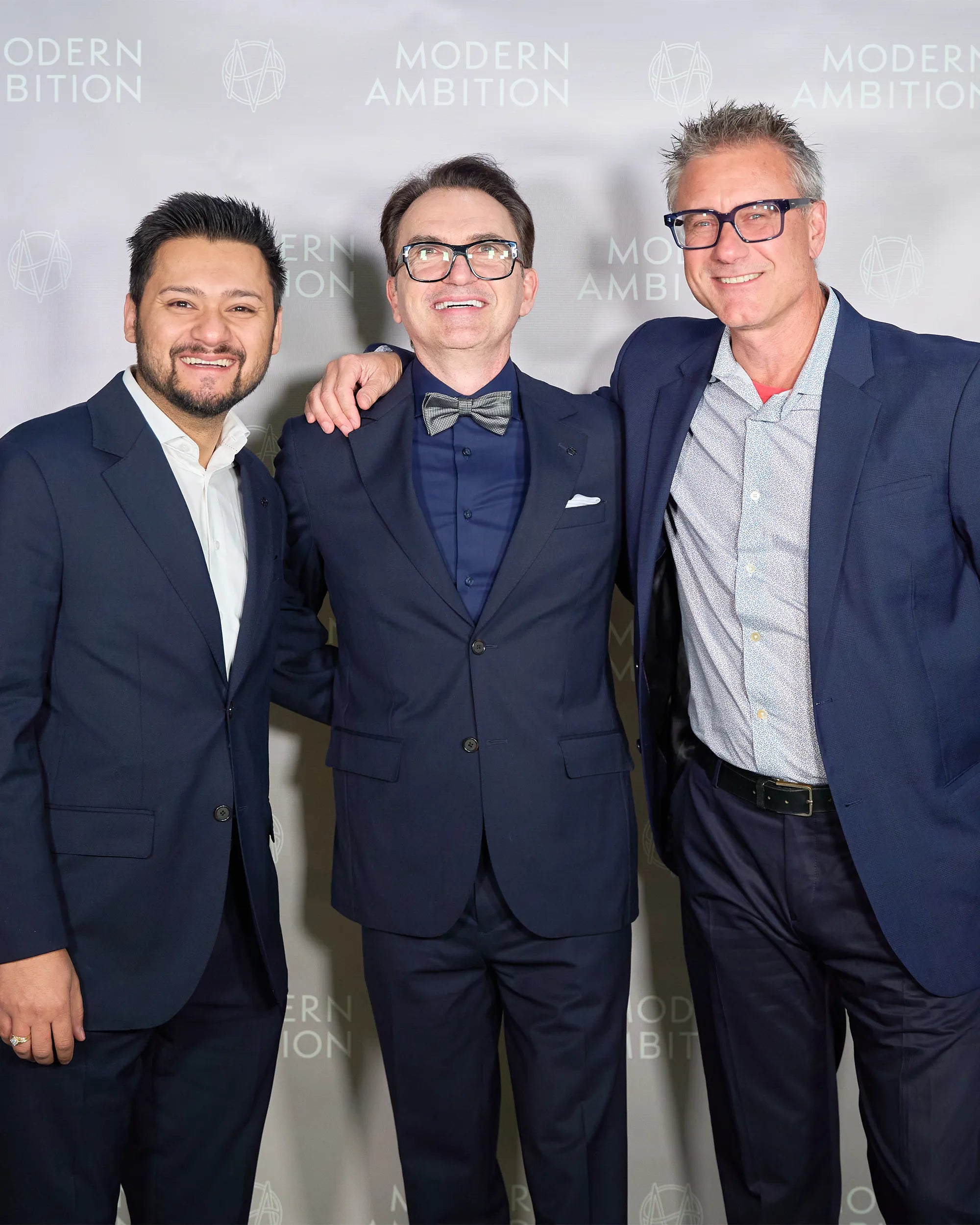 Three men in suits posing together against a branded backdrop