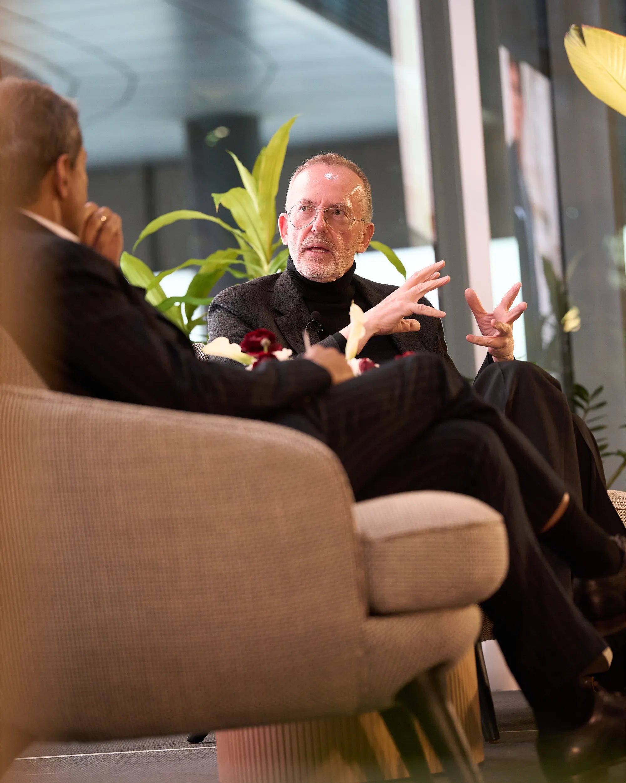 Two men engaged in a conversation in a modern indoor setting with plants.