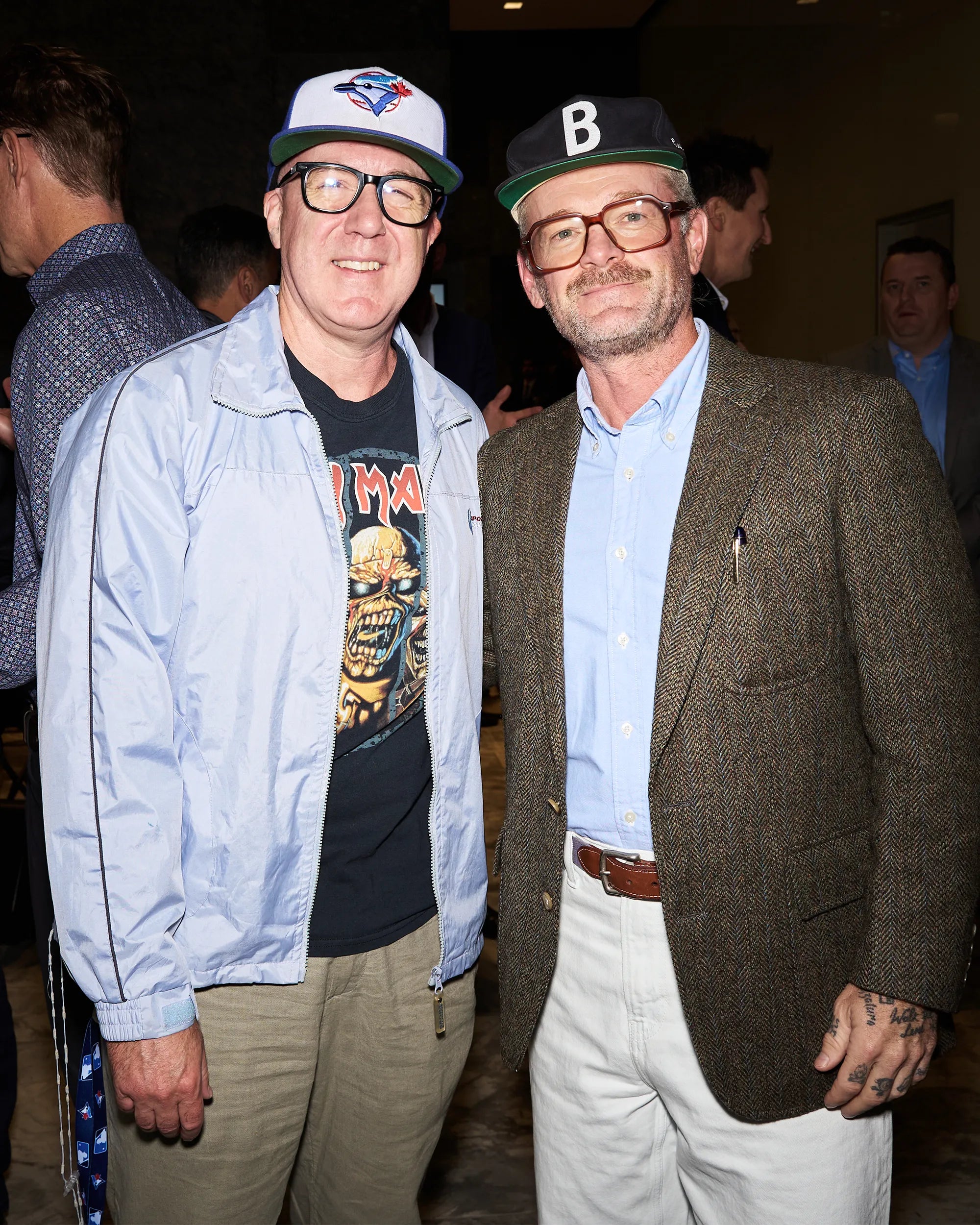 Two men standing together at an event, one wearing a light blue jacket and the other in a brown blazer.